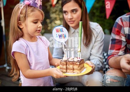 belle petite fille portant des tranches d'un gâteau d'anniversaire avec des bougies et des panneaux en carton « faire un souhait ». Anniversaire, célébration, fête Banque D'Images