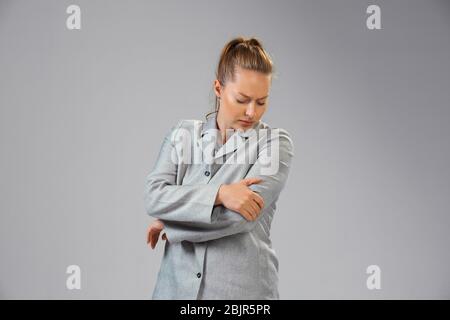 La jeune femme caucasienne souffre de douleurs coudées, se sent malade, malade et faiblesse isolérée sur fond gris de studio. Symptômes de malaise ou de style de vie malsain. Maladie, illidité, triste et bouleversée. CopySpace. Banque D'Images