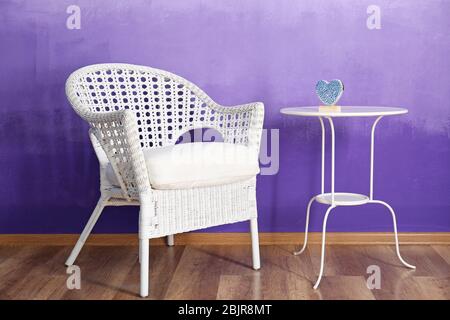 Fauteuil élégant en osier et table contre le mur violet Banque D'Images