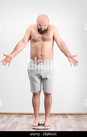 Homme en surpoids mesurant son poids à l'aide de balances sur le sol Banque D'Images