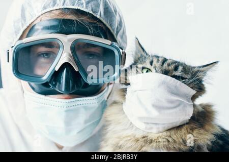 Médecin de l'homme dans des lunettes de protection avec les bras croisés et le chaton de chat est sûr du coronavirus dans le masque de protection médicale. Pandémie mondiale Banque D'Images