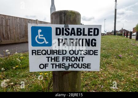 Un avis sur un court montant dans une verge d'herbe donne avis qu'un emplacement de stationnement à l'extérieur d'une maison est nécessaire comme une place de stationnement pour personnes handicapées. Banque D'Images