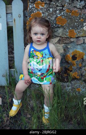 Jolie petite fille assise sur un mur de pierre, France Banque D'Images