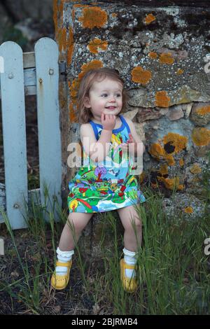 Jolie petite fille assise sur un mur de pierre, France Banque D'Images