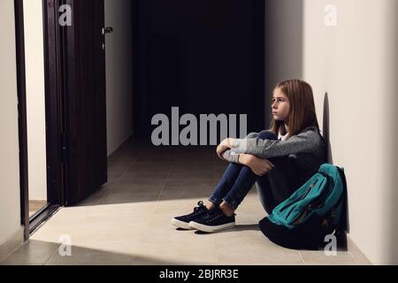 Une jeune fille triste assise au sol à l'intérieur Banque D'Images