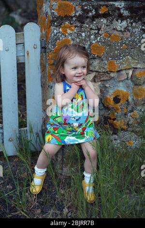 Jolie petite fille assise sur un mur de pierre, France Banque D'Images