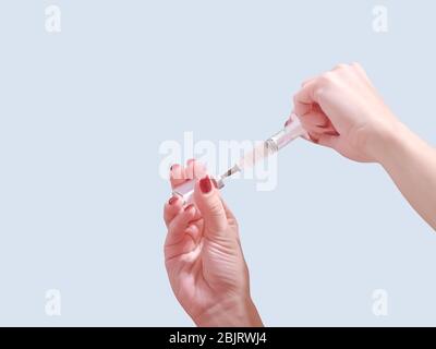 Une main avec des ongles rouges tient une seringue. Fille tient une seringue pour pointé. Médecine. Fond bleu froid, emplacement du texte. Banque D'Images