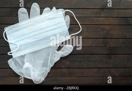 Masque médical blanc et gants jetables sur fond en bois sombre.Gants pour la protection contre le coronavirus. Banque D'Images
