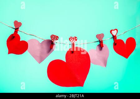 Coeurs en papier de clous de girolthons rouges avec un coeur sur une corde. Saint Valentin amour. Arrière-plan Aqua Menthe. Espace de copie Banque D'Images