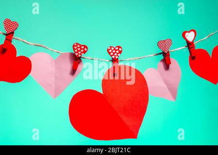 Coeurs en papier de clous de girolthons rouges avec un coeur sur une corde. Saint Valentin amour. Arrière-plan Aqua Menthe. Espace de copie Banque D'Images
