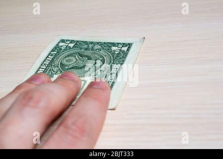 la main tient une facture d'un dollar sur une table en bois clair. vue latérale. pour fermer Banque D'Images