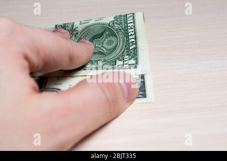 la main tient une facture d'un dollar sur une table en bois clair. vue latérale. pour fermer Banque D'Images