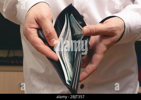 man montre un portefeuille avec un paquet de factures de cent dollars dans une chemise blanche au bureau Banque D'Images