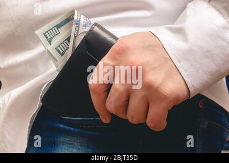 un homme pose un sac à main dans sa poche avant jean un paquet de billets de cent dollars dans une chemise blanche au bureau Banque D'Images