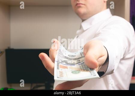L'homme caucasien tient à la caméra un lot de factures de cent dollars dans une chemise blanche au bureau Banque D'Images