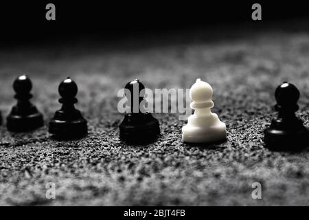 une rangée de pions noirs et un pion blanc parmi ses étrangers sur le béton noir un fond sombre. espace de copie Banque D'Images