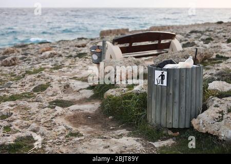 Poubelle pleine ou poubelle avec bouteille en plastique, canette à bière et déchets organiques Visibile montrant la pollution dans les zones côtières près de la mer. Banc en bois avec Banque D'Images