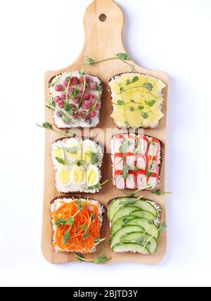 Six sandwichs sur pain grillé avec carottes fraîches, concombres, ananas, cassis rouge, bâtonnets de crabe et œufs de caille avec microgreens de pois sur planche en bois Banque D'Images