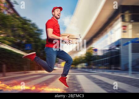 Messenger en uniforme rouge fonctionne à pied très rapidement pour livrer rapidement des pizzas chaudes juste cuites Banque D'Images