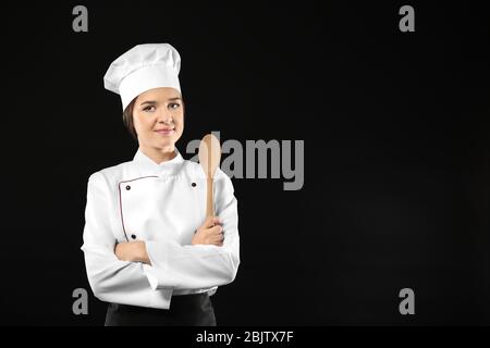 Portrait de chef femelle avec cuillère en bois sur fond noir Banque D'Images
