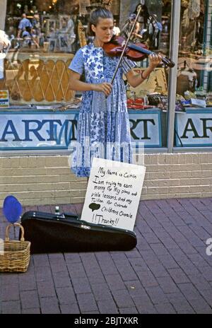 Un musicien de rue qui a été en bus à Denver, Colorado, États-Unis c. 1965. Elle joue un violon et un panneau écrit à la main à ses pieds nous dit qu'elle est appelée Caitlin et qu'elle est en train de prendre de l'argent pour payer des leçons de piano et de violette plus des frais de scolarité pour la chorale des Childrens du Colorado. Elle a également dessiné un grand cœur sur lui. Banque D'Images