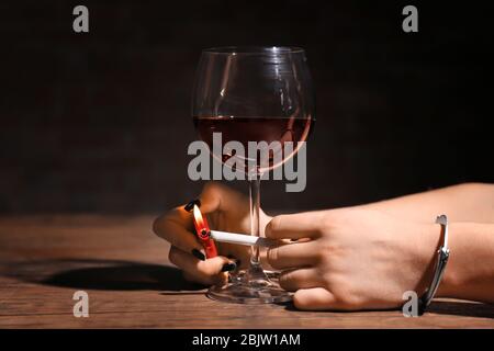 Femme aux menottes éclairant la cigarette près d'un verre de vin. Alcoolisme et dépendance à la nicotine Banque D'Images