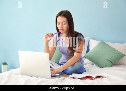 Jolie fille adolescente utilisant un ordinateur portable pendant ses devoirs dans la chambre Banque D'Images