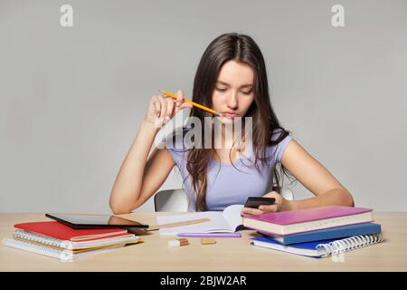 Jolie fille adolescente faisant des devoirs sur fond gris Banque D'Images