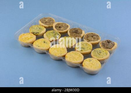 Mini épinards surgelés florentine, quiches au fromage et aux champignons dans un emballage en plastique sur fond bleu Banque D'Images