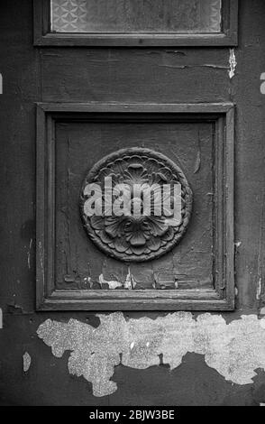 Photo en noir et blanc de l'élément de travail architectural de l'ancienne porte en bois avec peinture écaillée. Rosette sculpturale dans le cadre carré du panneau de porte de cla Banque D'Images