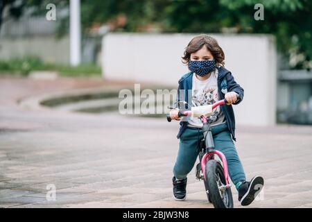 Magnifique enfant sur un vélo avec un masque pour éviter de répandre le coronavirus Banque D'Images