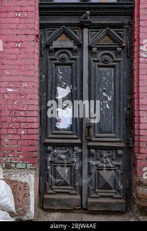 Entrée à l'édifice historique abandonné avec une ancienne porte endommagée de panneaux noirs ornés sur le mur de briques rouges. Architecture ruinée de la ville européenne Banque D'Images