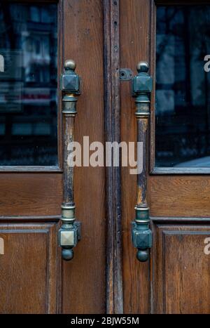 Poignées de portes en métal vintage orné de portes doubles en bois vieillies dans la ville européenne. Poignées symétriques et texture en bois sombre de la vieille porte avec un effet flou Banque D'Images