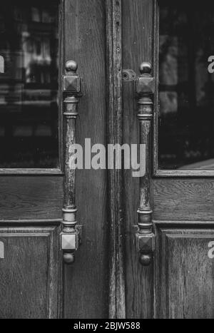 Photo en noir et blanc des poignées de portes en métal vintage orné de double porte en bois dans la ville européenne. Poignées symétriques et texture en bois de l'ancienne porte avec Banque D'Images