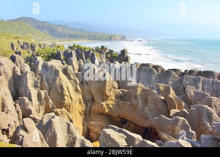 Côte pittoresque avec des formations rocheuses sauvages appelées Pancake Rocks à Punakaiki en Nouvelle-Zélande avec une belle longue plage en arrière-plan. Banque D'Images