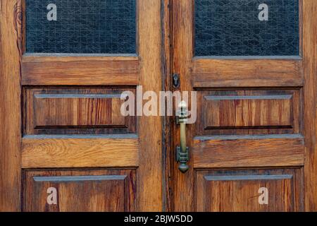 Panneaux de portes doubles en bois avec fenêtres rectangulaires et cadres intérieurs en verre mat. Bouton de porte rétro et serrure de serrure ancienne sur la surface en bois de grunge fermer Banque D'Images