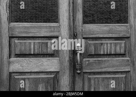 Photo en noir et blanc des panneaux de portes doubles en bois avec fenêtres rectangulaires et verre mat à motifs à l'intérieur des cadres. Bouton de porte rétro et trou de serrure en ol Banque D'Images