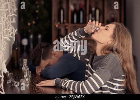 Jeune femme buvant près de l'homme ivre inconscient au bar. Problème d'alcoolisme Banque D'Images