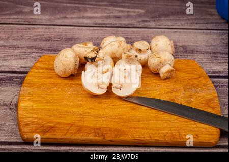 Moitiés de champignons coupés et de jeunes champignons dispersés sur fond de bois. Gros plan Banque D'Images