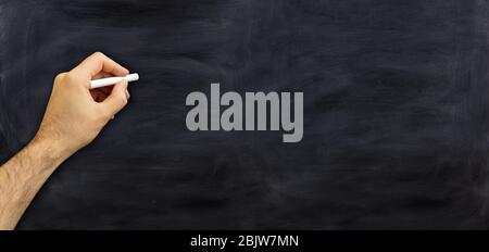 Main gauche tenant une craie isolée sur fond noir. Homme gaucher contre un tableau de surveillance, espace de copie, bannière Banque D'Images