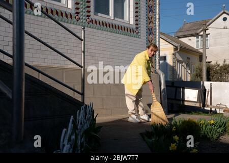 Femme en chemise jaune balayant véranda arrière-cour nettoyage pile Banque D'Images