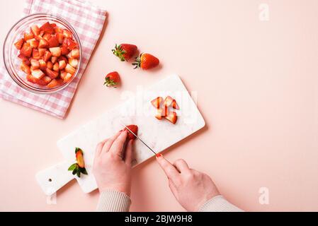 Femme à la main, sur une table rose, trancher les fruits de fraise sur un tableau de découpe. Plat avec la fabrication de confiture de fraises. Faire de la marmalade à la maison. Banque D'Images