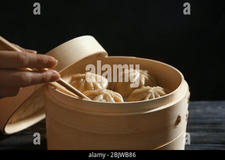 Femme tenant baozi haletant avec des baguettes près du cuiseur vapeur en bambou, ferme Banque D'Images