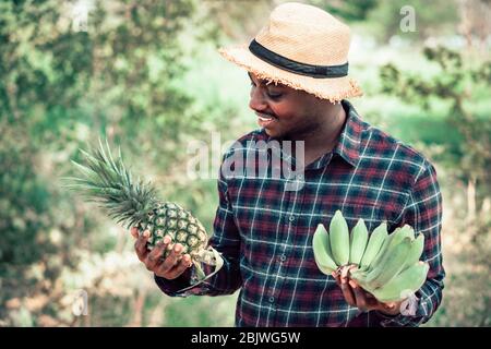 Cultivateur africain tenant l'ananas et la banane à la ferme biologique avec sourire et heureux.Agriculture ou concept de culture Banque D'Images