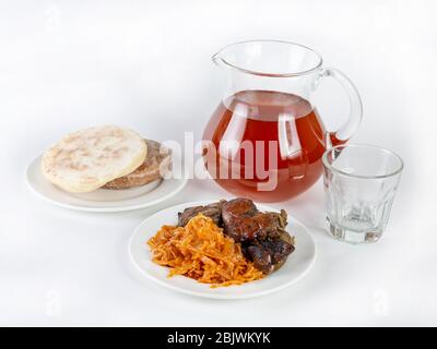 Une portion de foie de boeuf frit avec des légumes cuits à côté de gâteaux de pain et une verseuse en verre de boisson aux baies sur fond blanc Banque D'Images