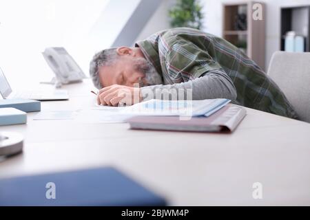 Homme senior fatigué allongé sur la table au travail au bureau Banque D'Images