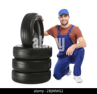 Jeune mécanicien en uniforme avec pneus de voiture sur fond blanc Banque D'Images
