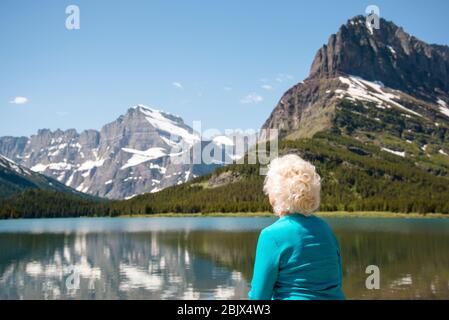 Femme âgée qui regarde loin de l'appareil photo dans le paysage de montagne du Montana. Parc national de Blond Hair Glacier, âgé de 70 ans, lieu de copie destination pittoresque. Banque D'Images