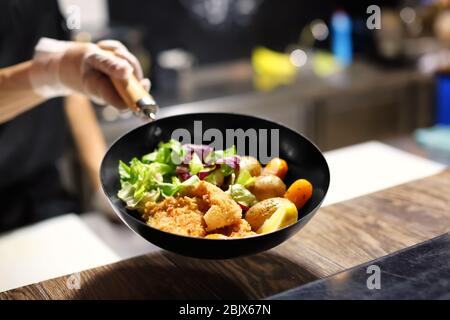 Chef tenant la poêle avec de délicieux filets de poisson et légumes dans la cuisine du restaurant Banque D'Images