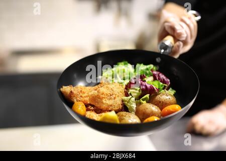 Chef tenant la poêle avec de délicieux filets de poisson et légumes dans la cuisine du restaurant Banque D'Images